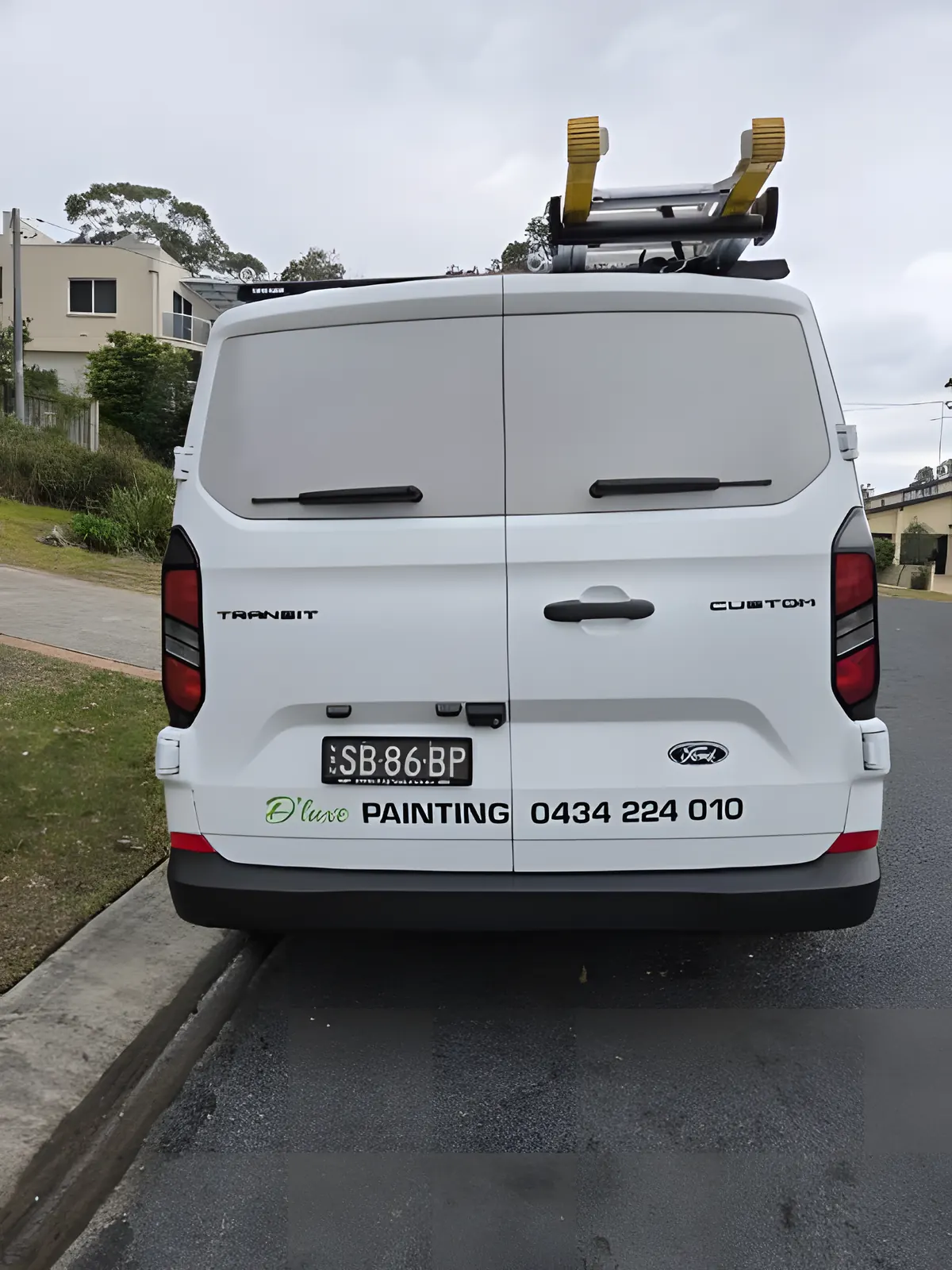 The D'luxe Painting van with ladders on the roof, parked at a job